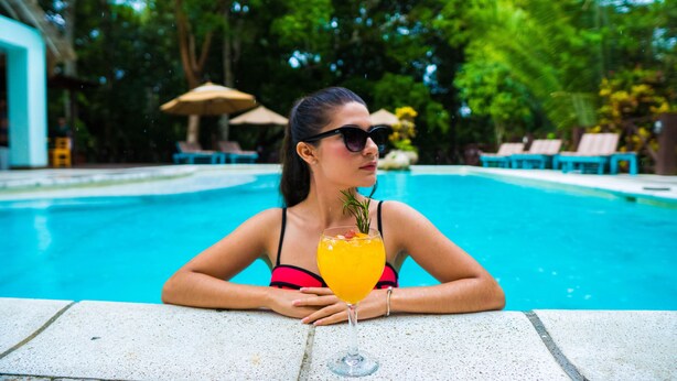A person sitting by a pool with a drink, surrounded by lounge chairs and umbrellas. - Hostal Jungle Lodge Tikal (Flores)