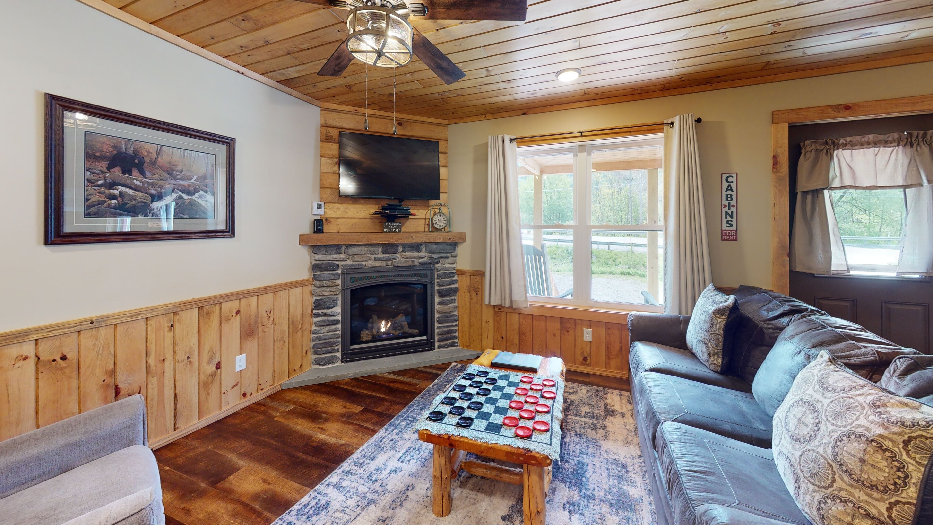 Un salón acogedor con chimenea, un televisor grande montado encima y un techo de madera, además de un sofá cómodo.