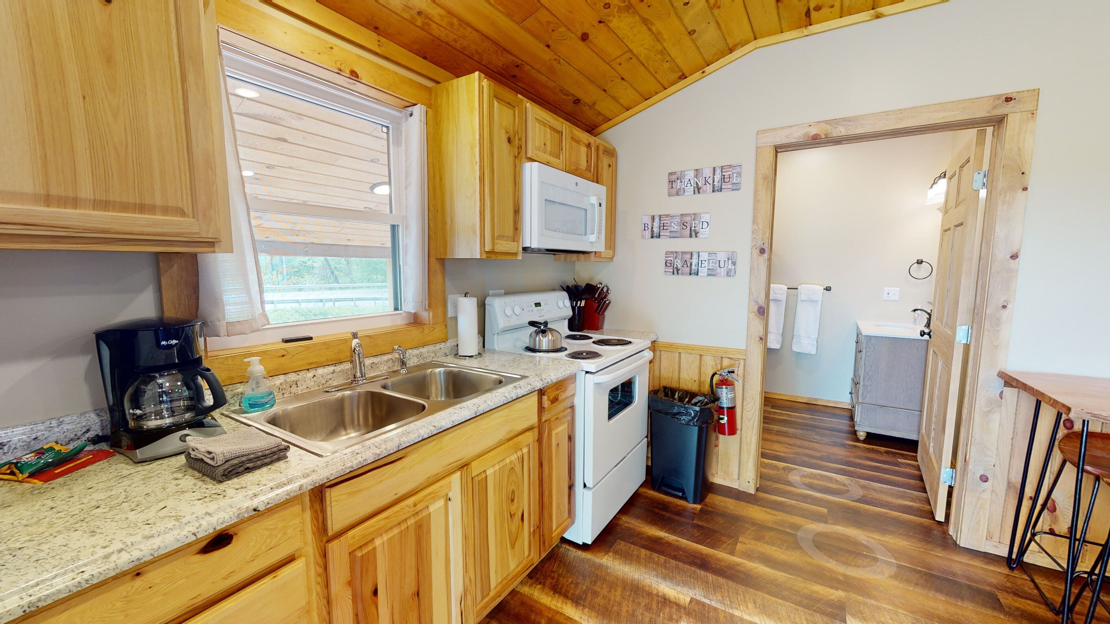 Une cuisine avec des meubles de rangement en bois, un fourneau blanc, un four à micro-ondes et une fenêtre avec des stores.
