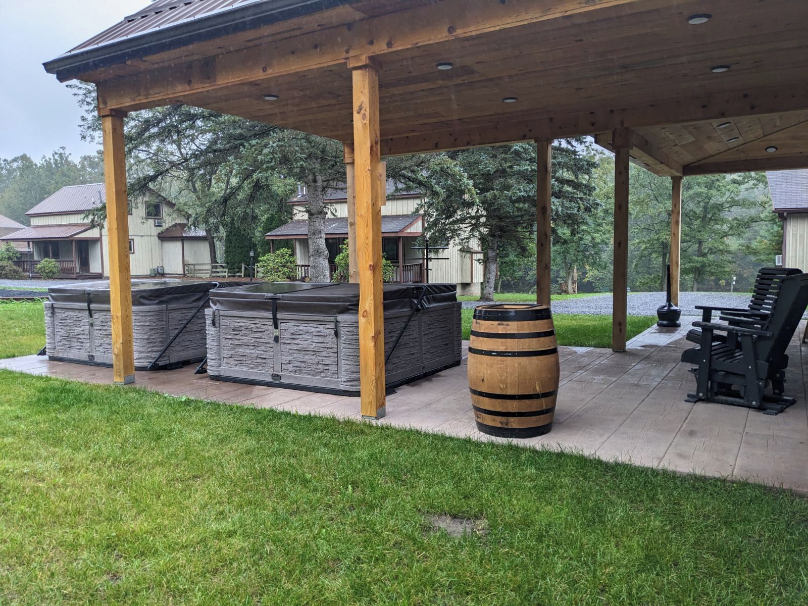 A covered patio area with a stone barbecue station, a wooden barrel, and outdoor seating.