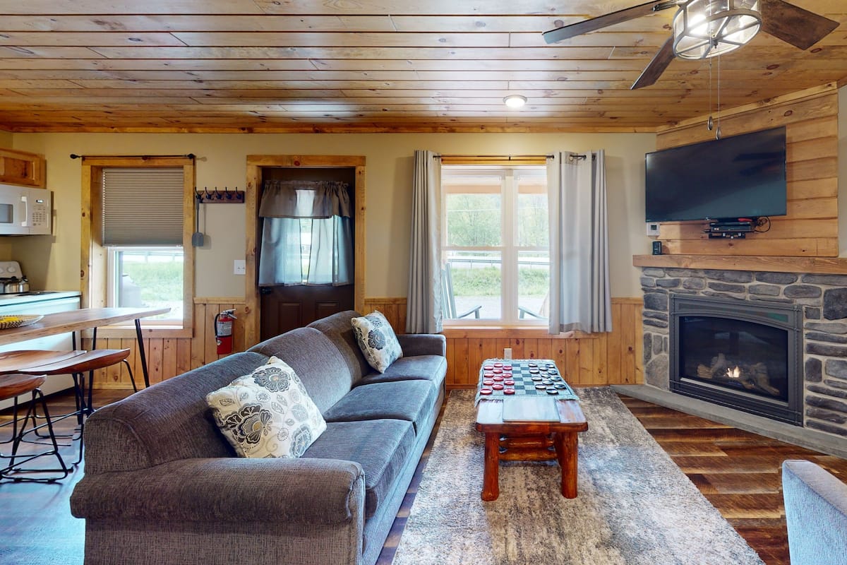 A cozy living room with a stone fireplace, a large flat-screen TV, and a wooden ceiling.