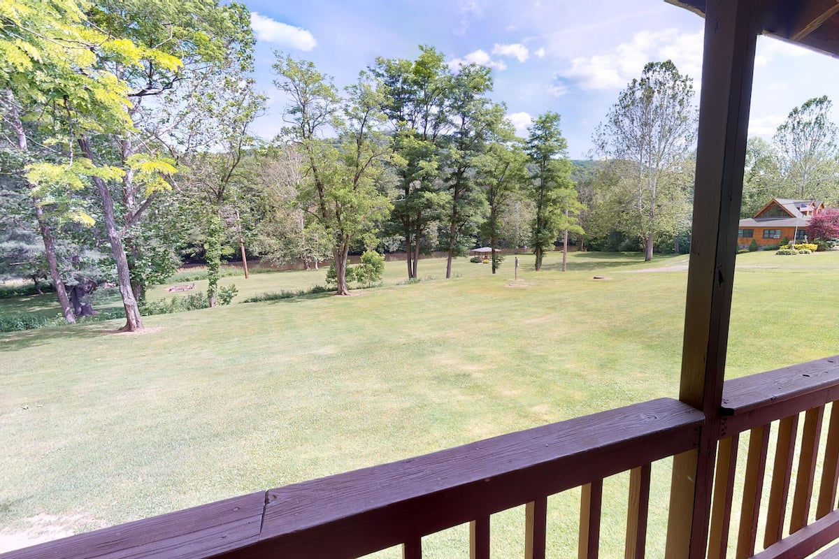 A view from a wooden deck overlooking a grassy yard with trees and a house in the background.