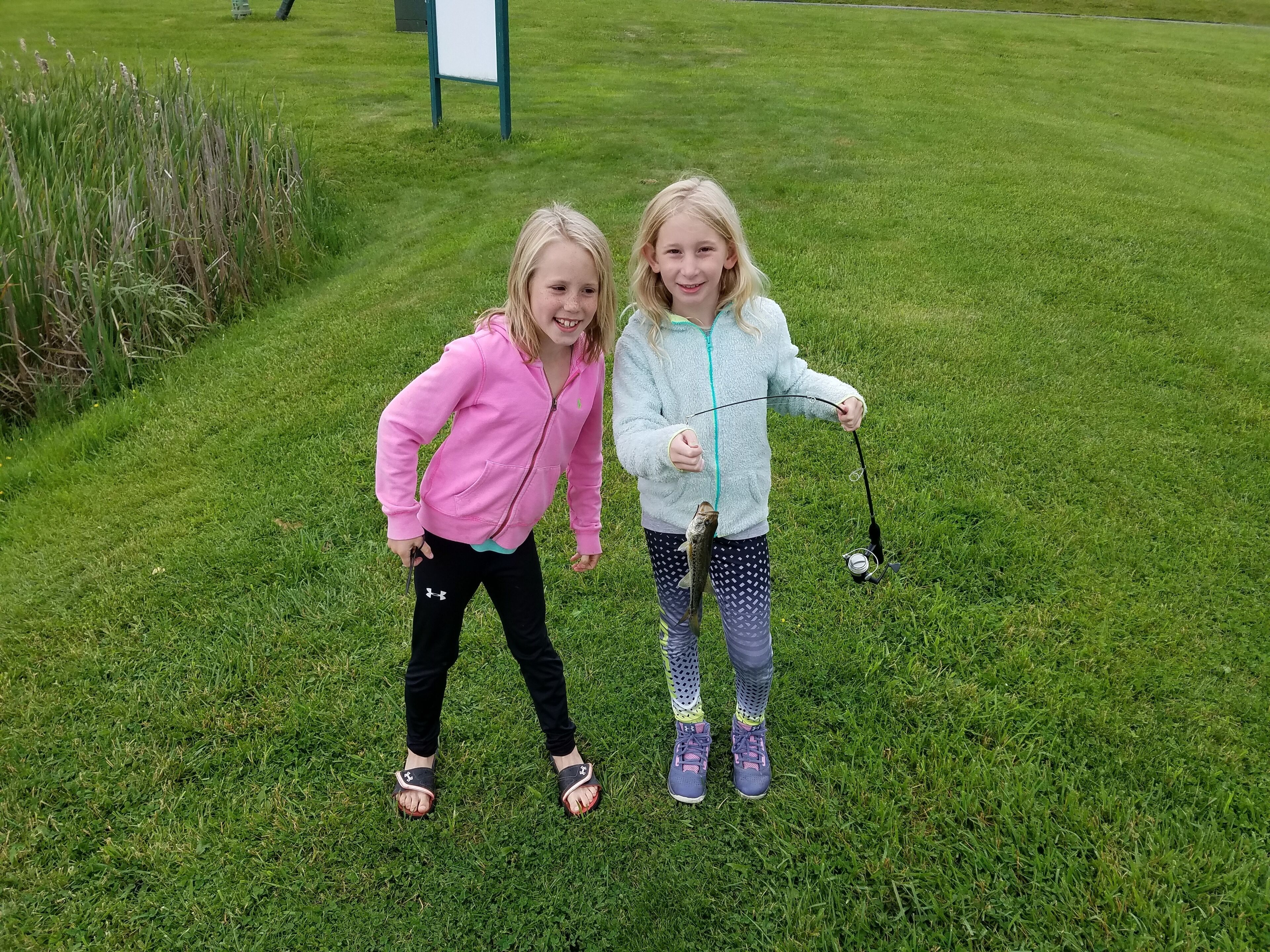 Two children standing on grass with a golf club and a ball.