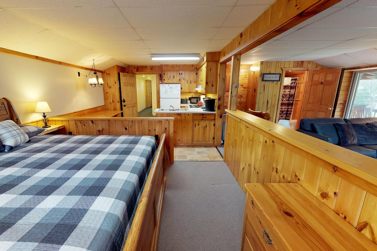 A cozy cabin interior with a bed, a sofa, a kitchenette, and a wooden exterior wall.