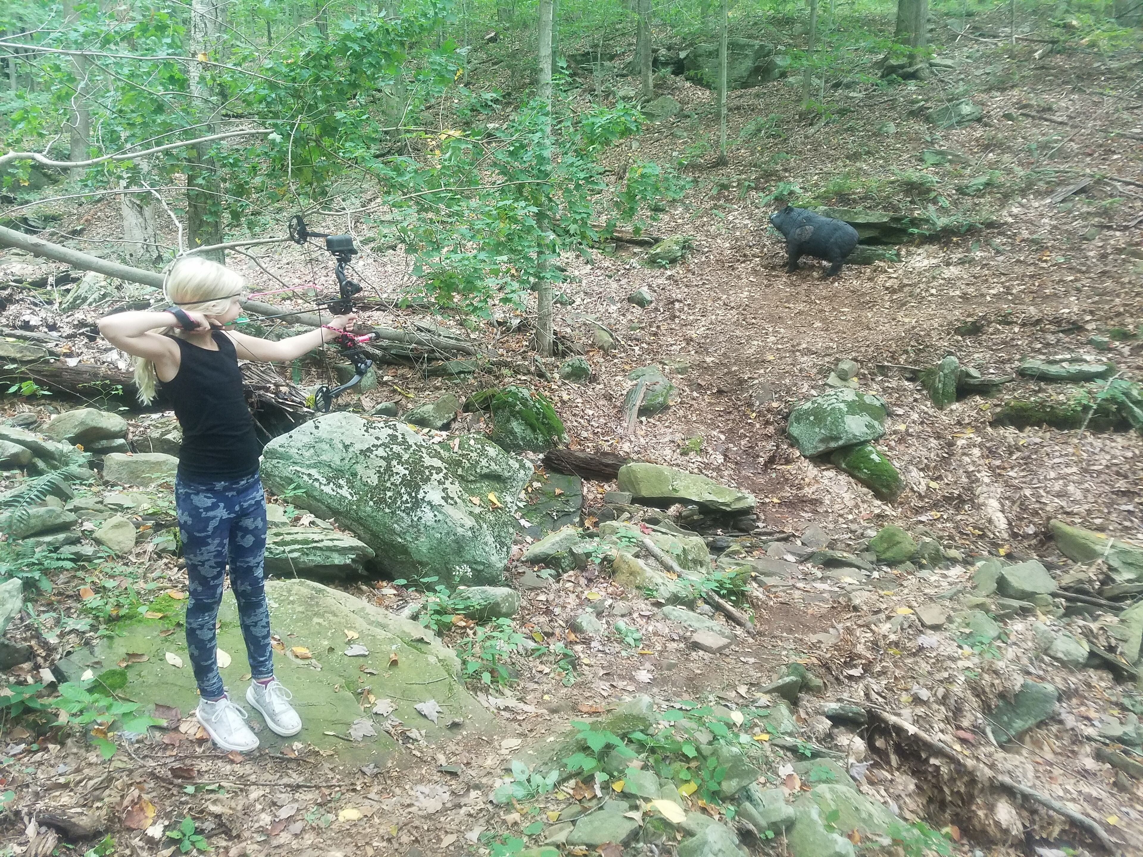 A person with a camera, standing on a rocky path in a forest.
