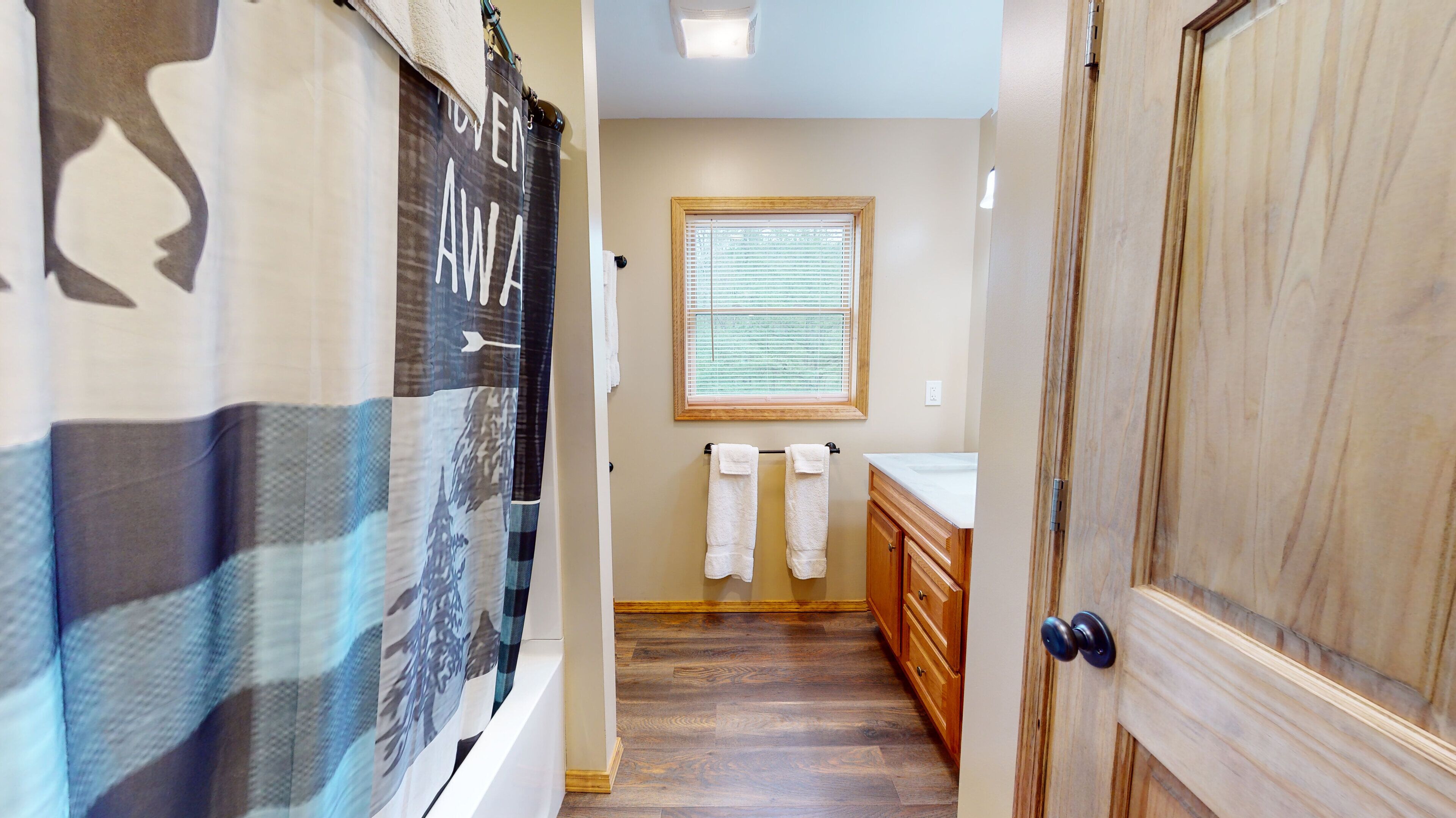 A hallway with a wooden door, a window with blinds, a towel rack with towels, and a wall with a poster.