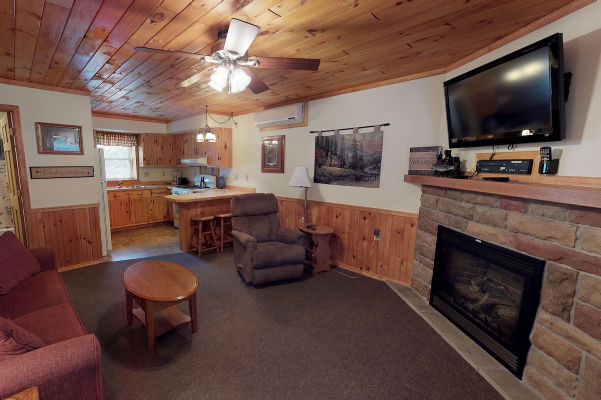 A cozy living room with a fireplace, a television, and a kitchen in the background.