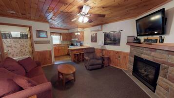 A cozy living room with a fireplace, a television, and a kitchen in the background.
