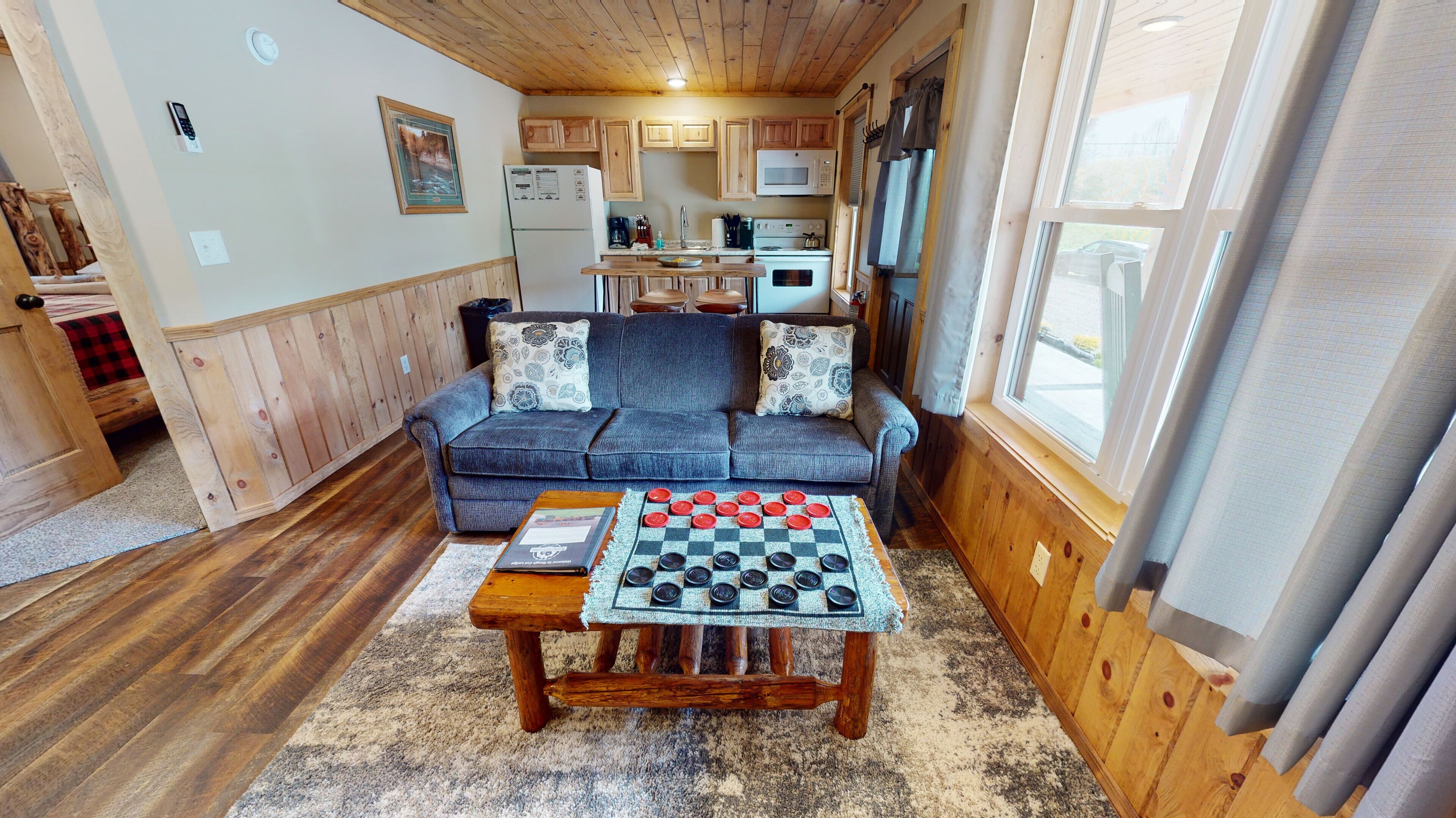 A cozy living room with a sofa, a coffee table with a checkered tablecloth, and a kitchen in the background.