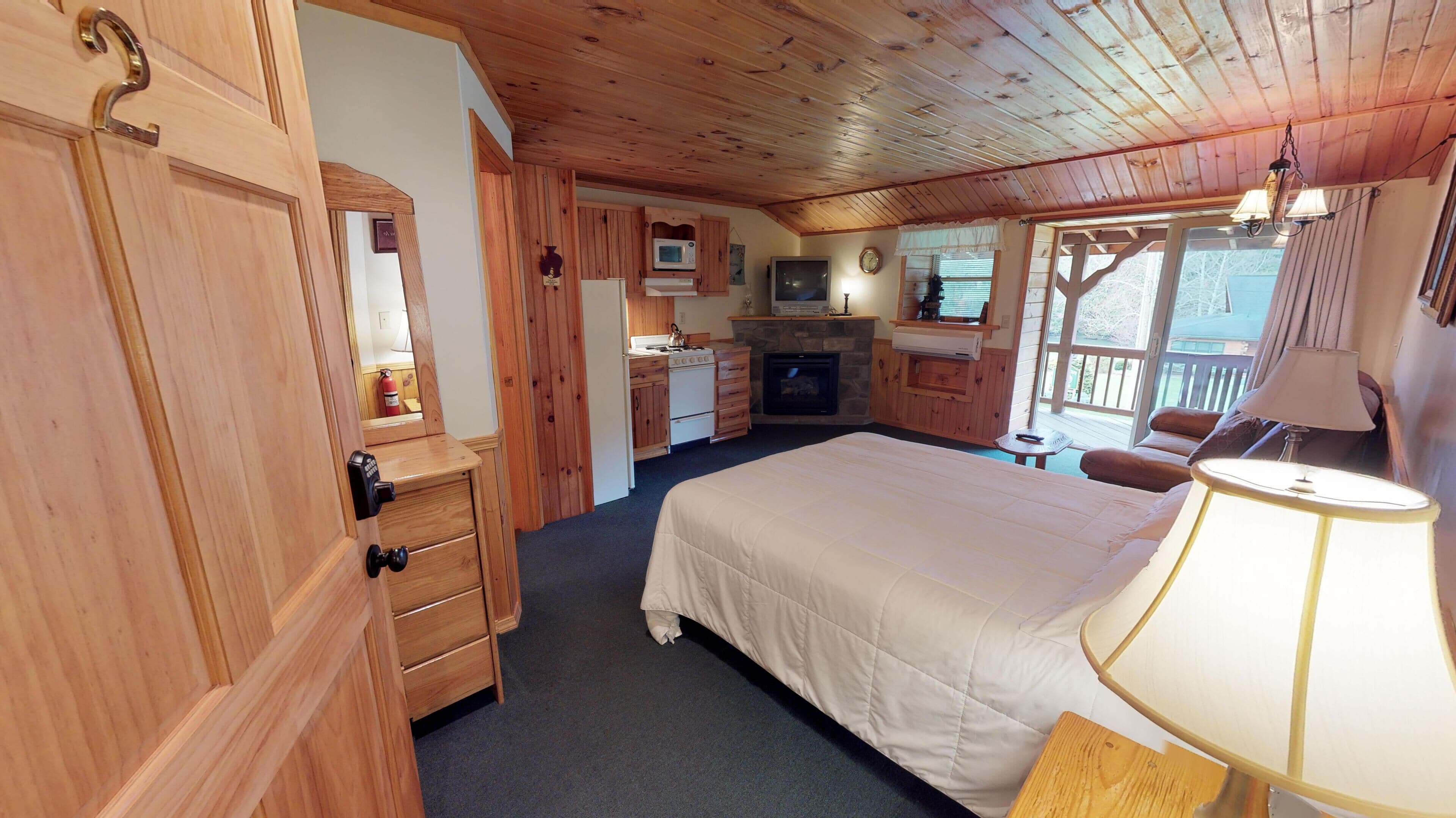 A cozy room with a bed, a wooden wardrobe, a kitchenette, and a fireplace.