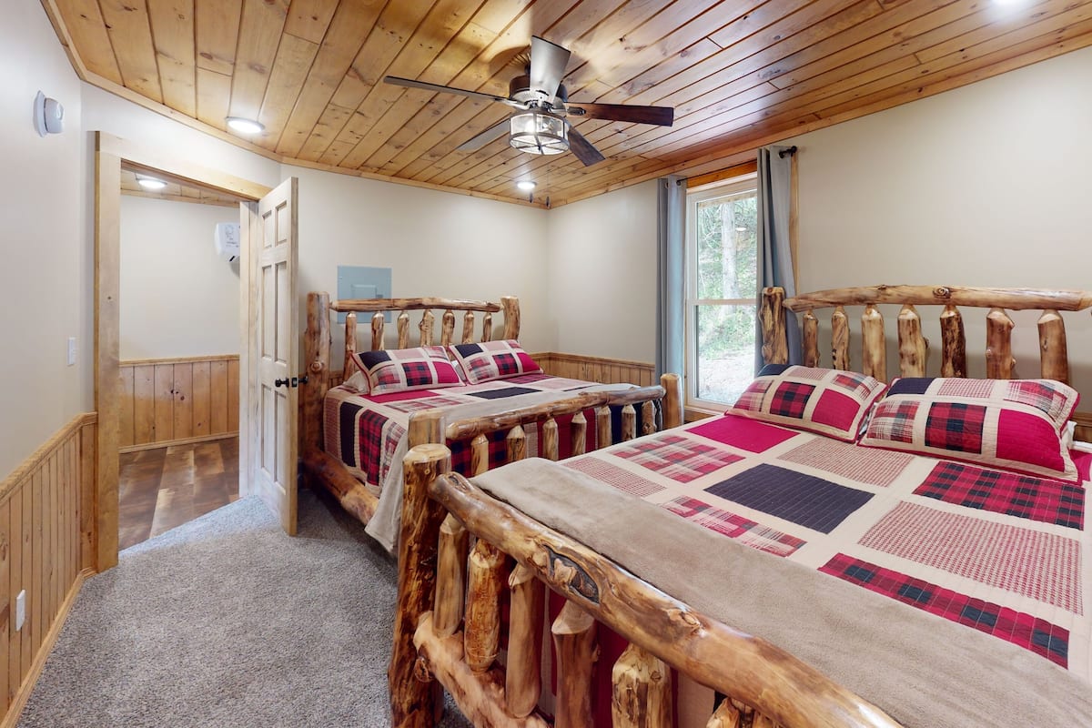 A bedroom with two wooden beds, a ceiling fan, and a window with curtains.