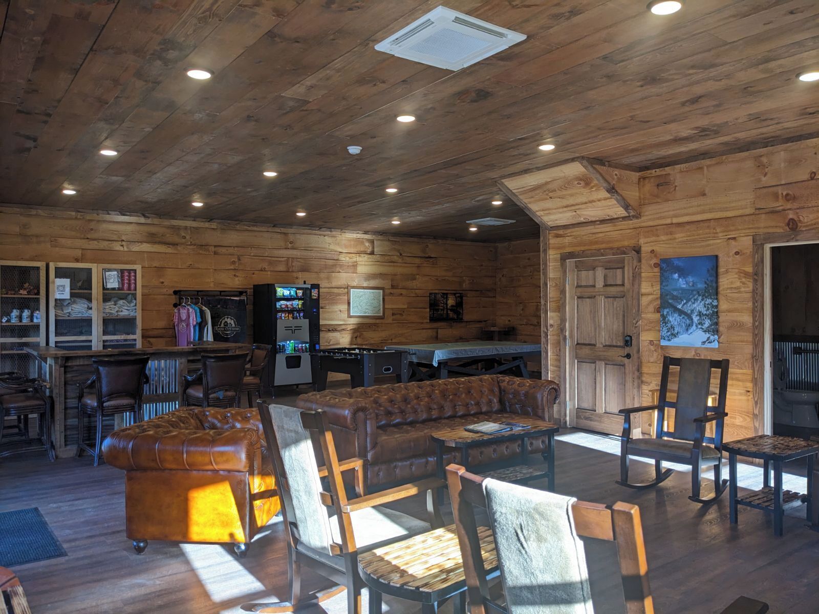Un interior rústico de madera con un sofá, sillas, una mesa de fútbol de mesa y un expendedor.