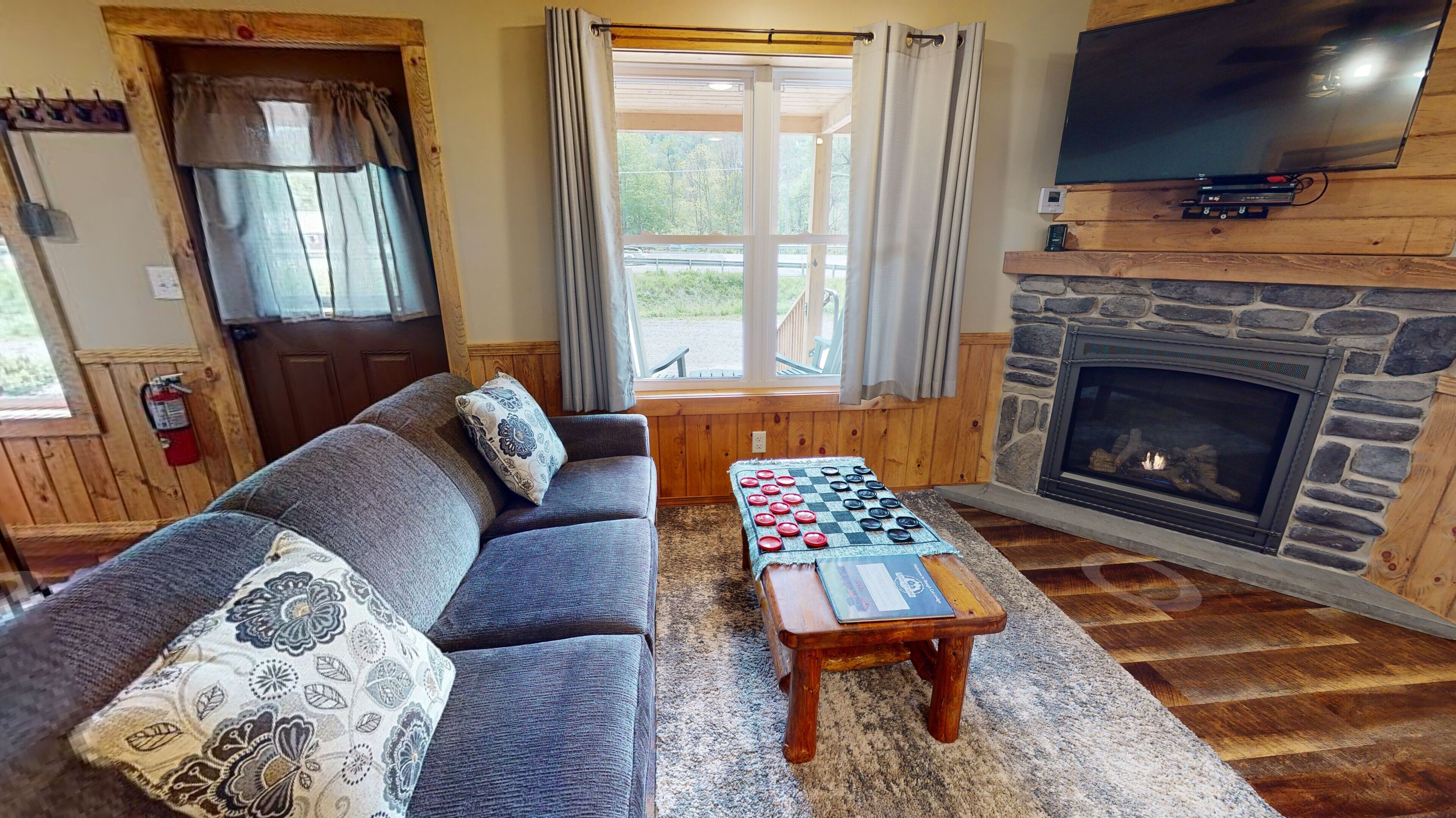 A cozy living room with a sofa, a checkers table, a fireplace, and a TV.