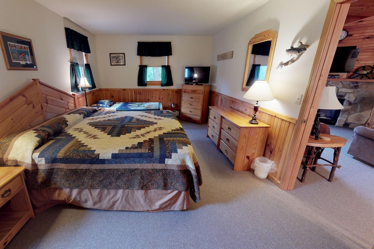 A bedroom with a wooden bed, a dresser, a nightstand, a lamp, a mirror, and a small table with a lamp.