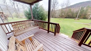 A wooden deck with a swing set and a view of a grassy area and trees.