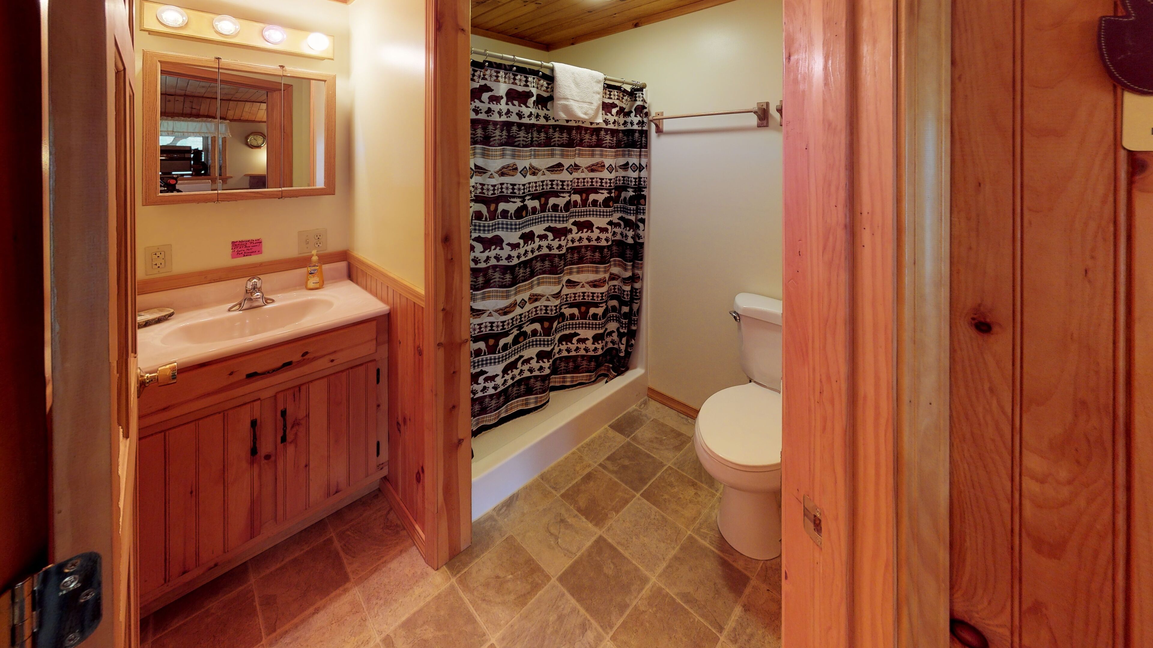 A bathroom with wooden cabinets, a sink, a toilet, and a shower curtain with animal prints.