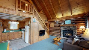 A cabin interior with a kitchen, living room, fireplace, and a staircase.