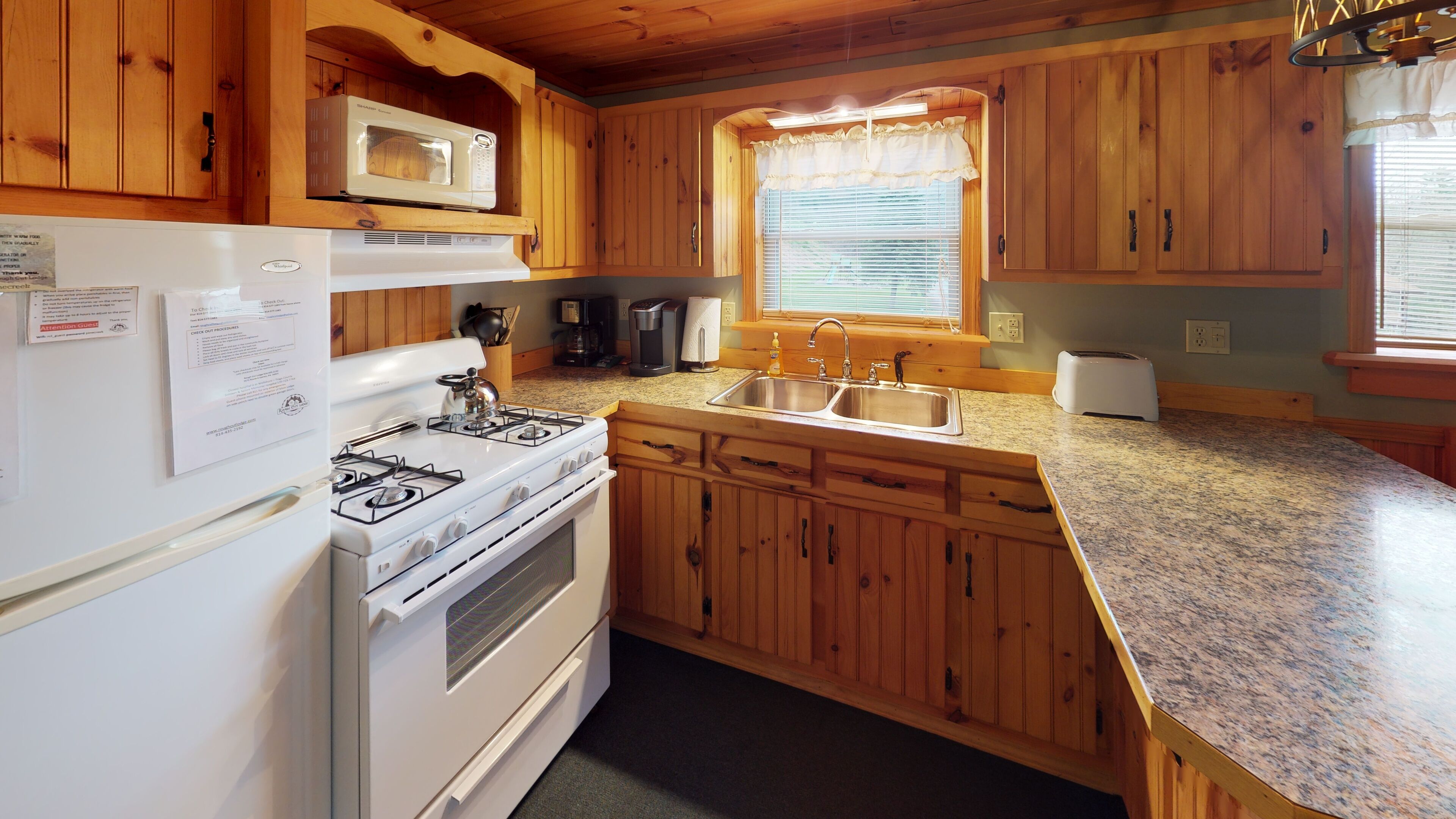 A kitchen with wooden cabinets, a white stove, a microwave, a sink, and a window with blinds.