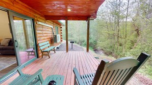 A wooden deck with benches and a table, overlooking a forested area.