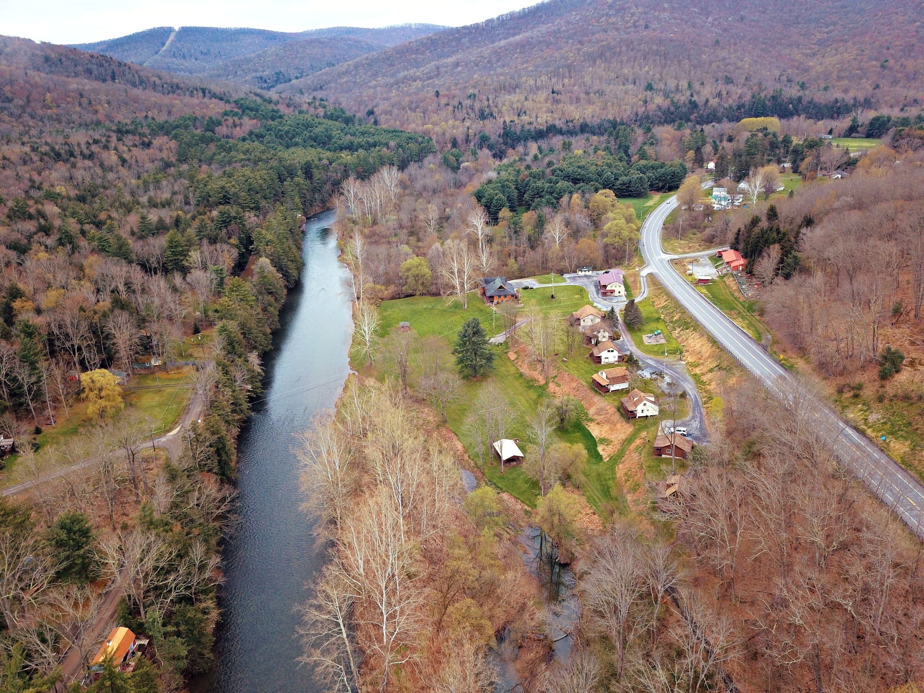 Vue aérienne d’une rivière qui traverse une vallée, avec des maisons sur la rive droite et une route qui serpente le long de la rivière.