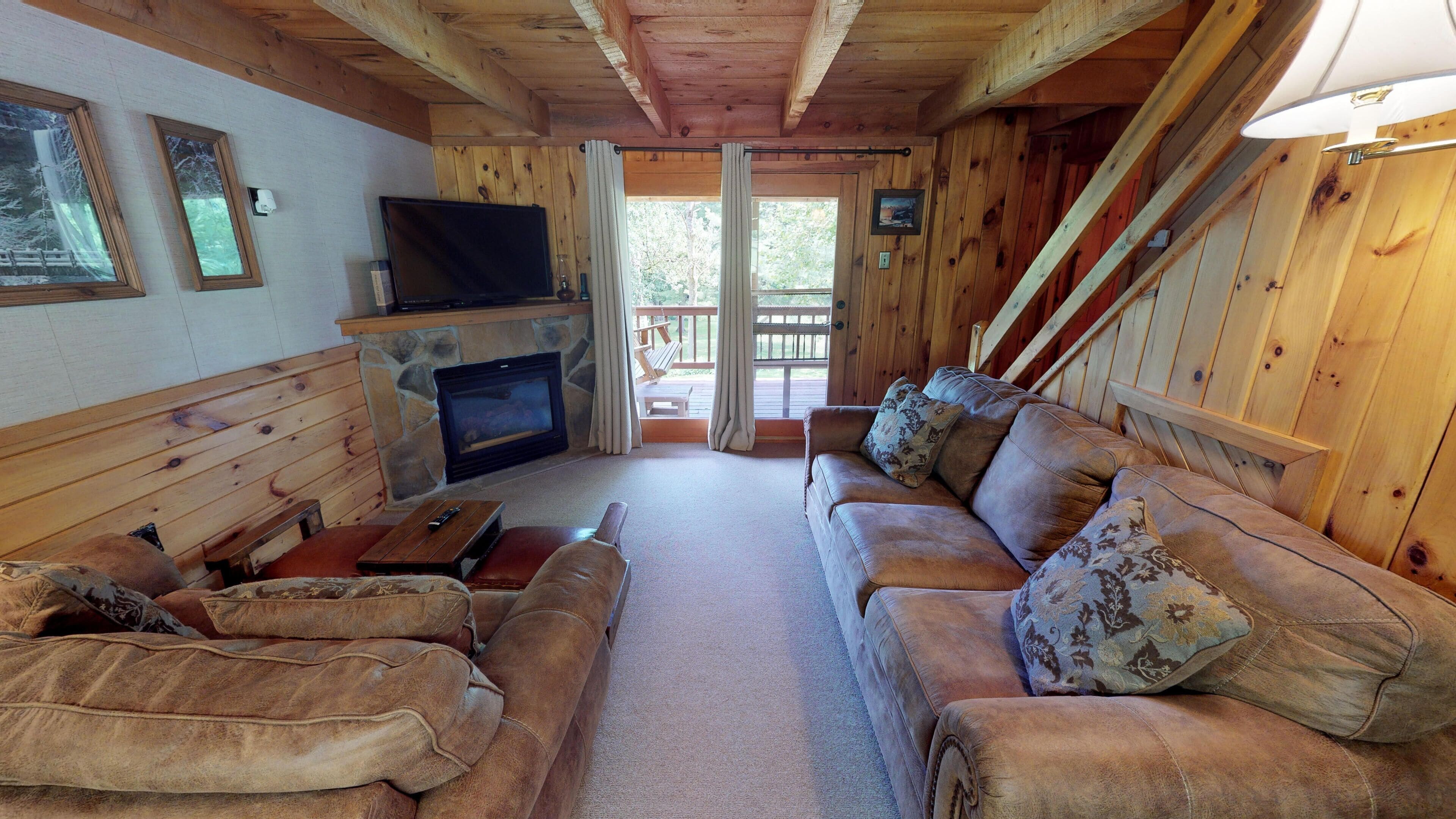 Interior acogedor de una cabaña con chimenea de piedra, paredes de madera, un sofá de cuero y un televisor.