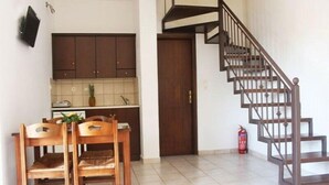 A kitchen with dark cabinets, a dining table with chairs, and a spiral staircase. - Lola Apartments (Platanias)