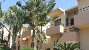 A multi-story residential building with balconies, surrounded by palm trees and other greenery. - Lola Apartments (Platanias)