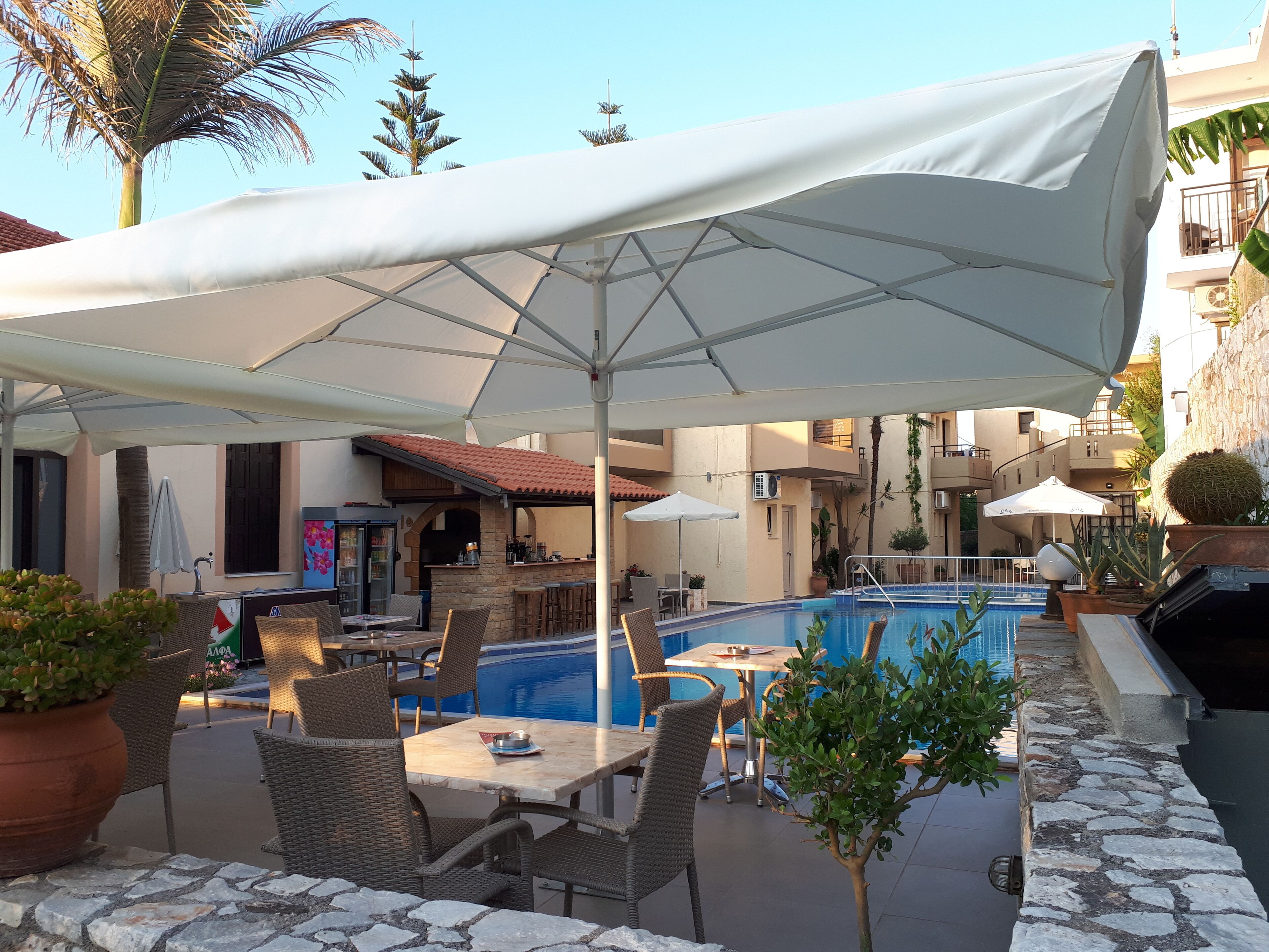 An outdoor pool area with a covered seating area, stone flooring, and a bar with a stone archway.