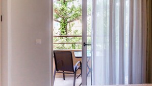 A hotel room with a bed, a chair, and a view of the outdoors through a door. - Lola Apartments (Platanias)