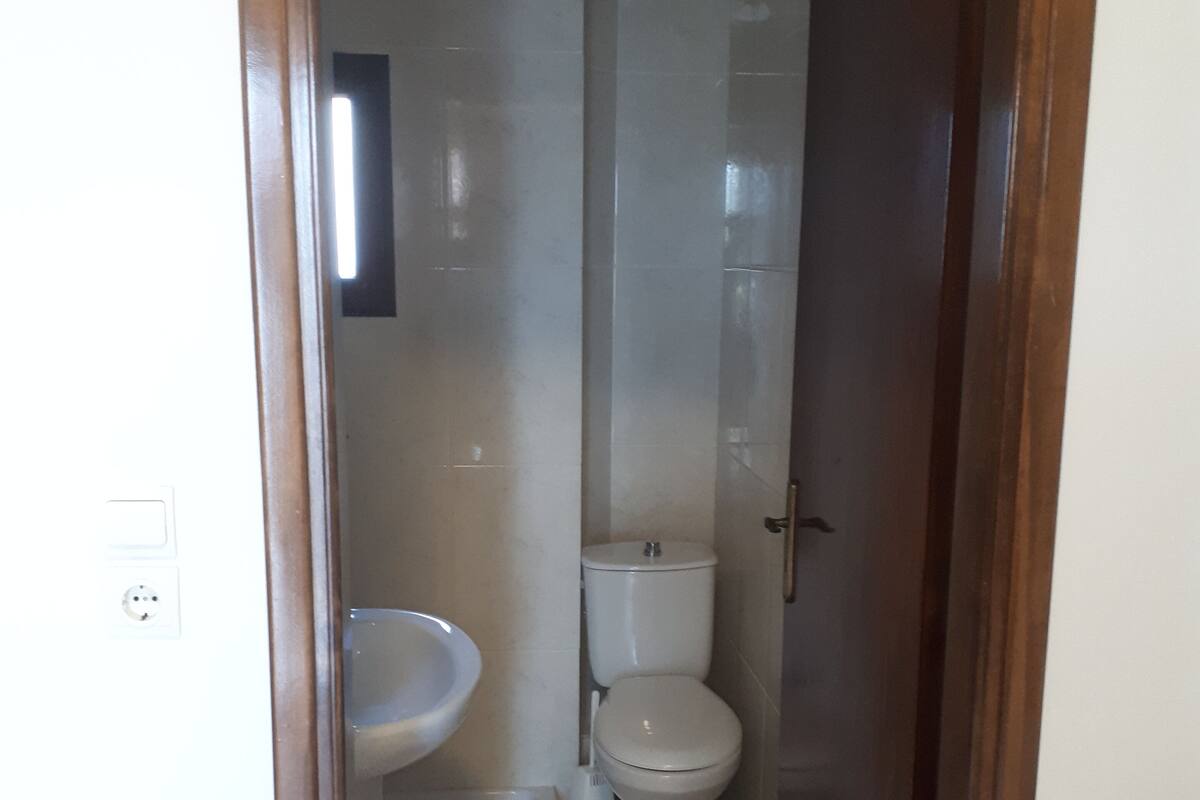 Um banheiro pequeno e estreito, com pia, vaso sanitário e área de chuveiro, tudo em branco.