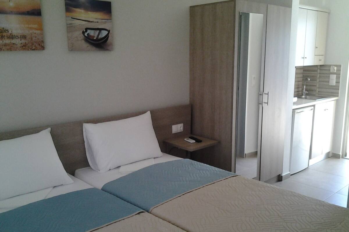 Quarto de hotel com cama, mesa de cabeceira, uma pequena mesa e área de cozinha compacta.