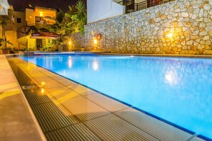 A swimming pool with a stone wall and a building in the background. - Lola Apartments (Platanias)