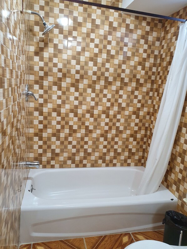 A bathroom with a checkered tile wall, a white bathtub, and a showerhead.