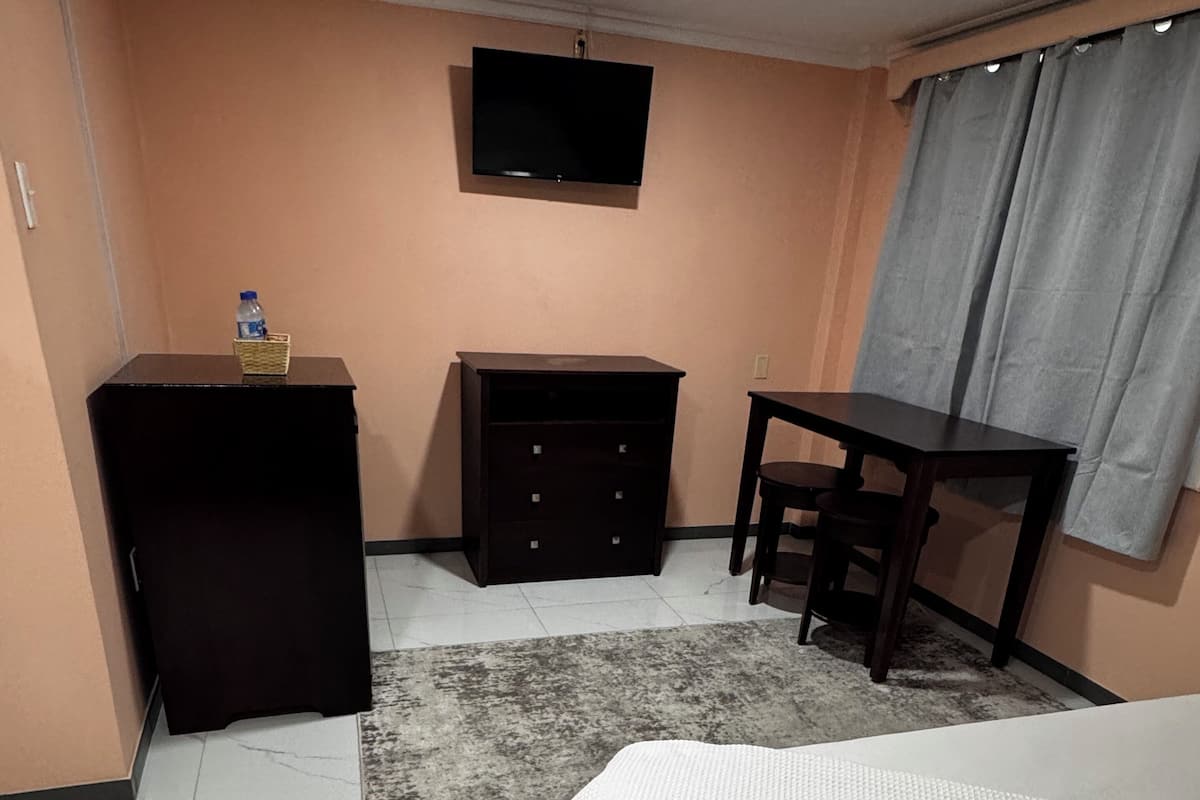 A bedroom with a bed, a desk, a wardrobe, and a television on the wall.