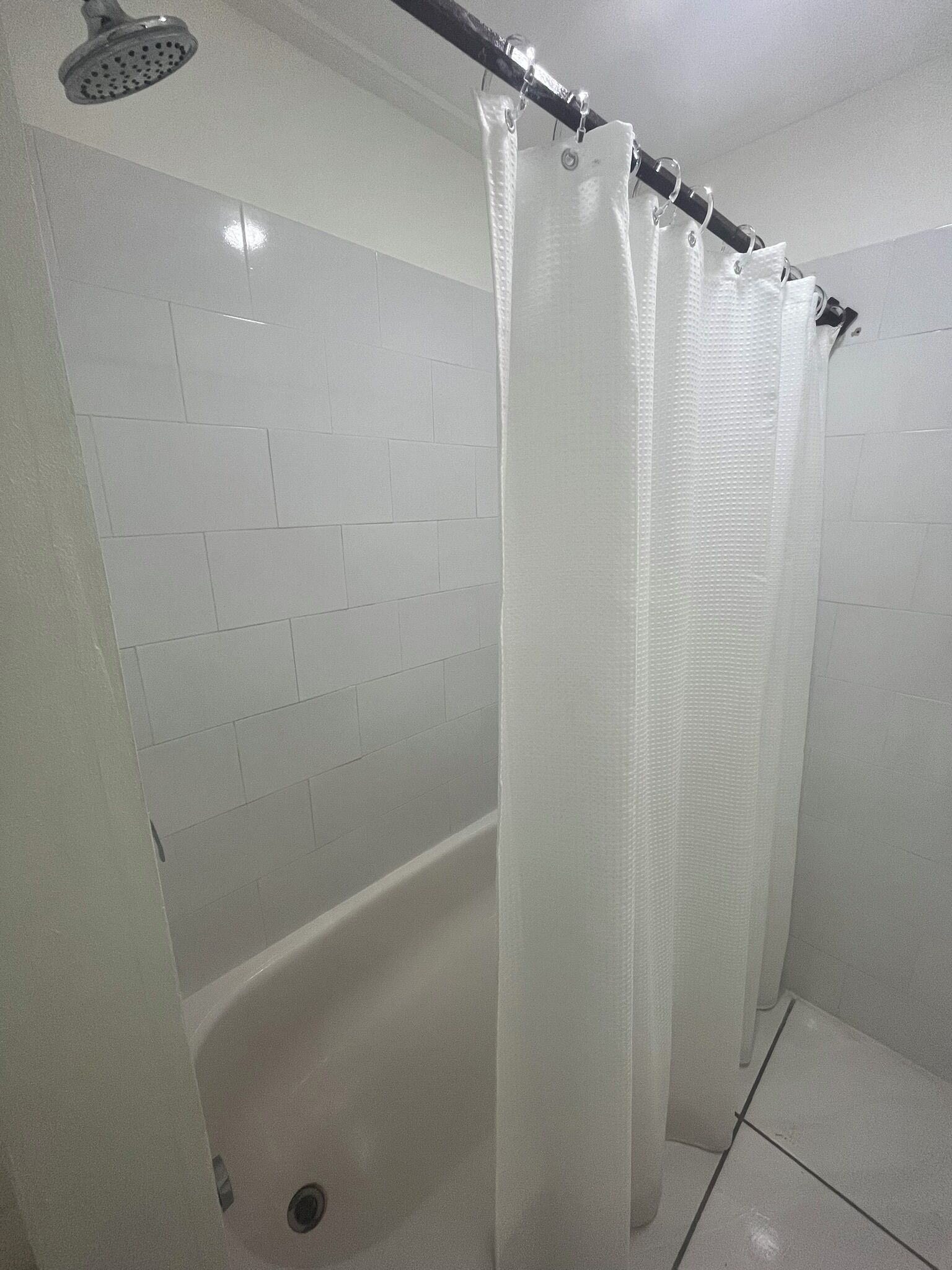 Un baño con paredes de azulejos blancos, una bañera y una cortina de ducha.