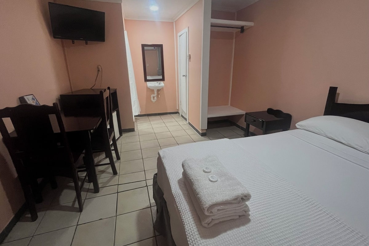 A hotel room with a bed, a desk, a chair, a TV, a bathroom, and a wardrobe.
