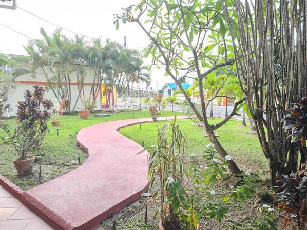 A garden with a curved pathway, various plants, and a building with a red roof in the background.