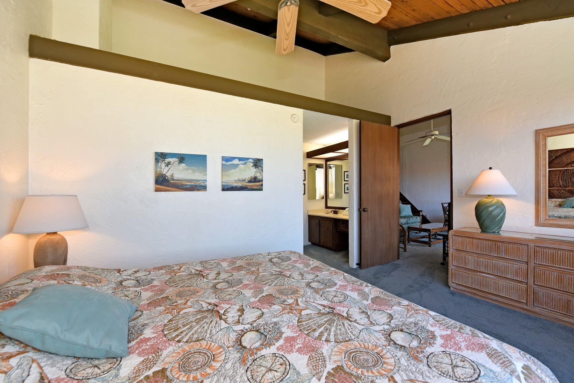 A bedroom with a bed, two wall-mounted paintings, a dresser, a mirror, and a door leading to another room.