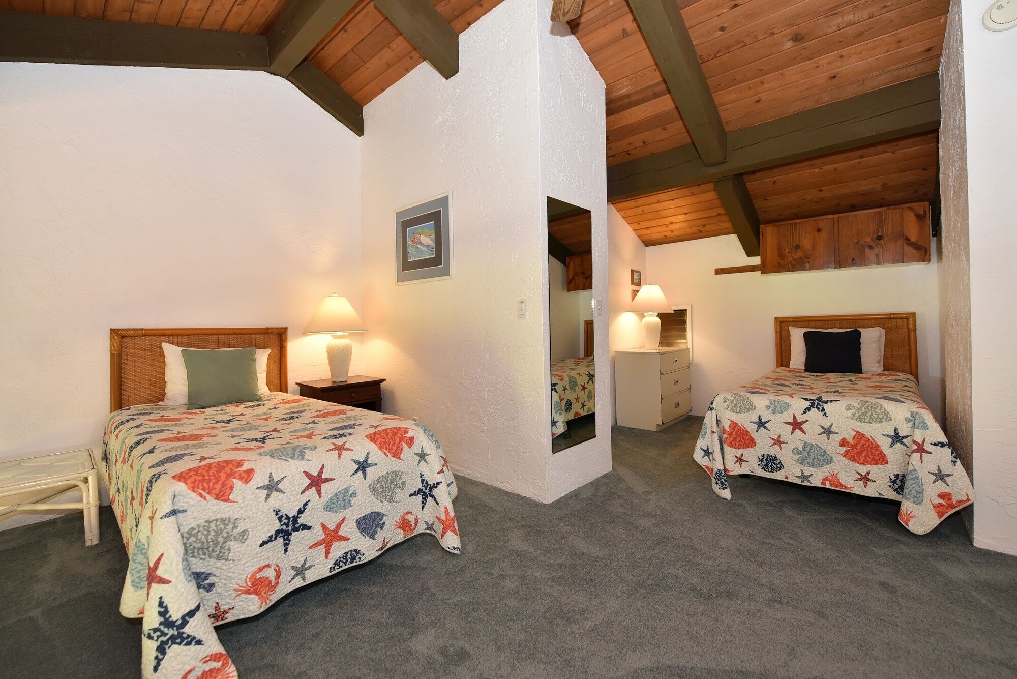 Une chambre avec deux lits, chacun recouvert d’une couvre-lit à motifs d’étoiles de mer, une table de chevet avec une lampe et un plafond en bois.