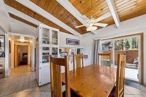 Uma área de refeições com mesa de madeira, cadeiras, ventilador de teto e vista para o exterior.