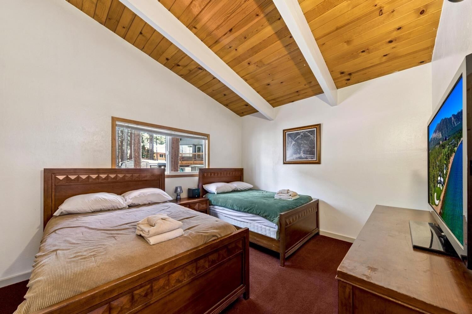 Ein Schlafzimmer mit zwei Holzbetten, einem Fernseher und einem Fenster mit Blick auf ein Gebäude.