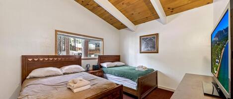 Un dormitorio con dos camas de madera, un televisor y una ventana con vistas a un edificio.