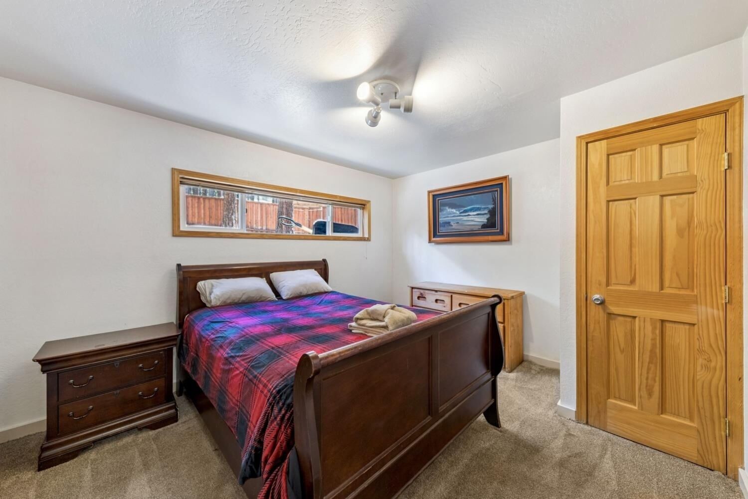 Une chambre à coucher comprenant un lit, une table de chevet, une commode, un ventilateur de plafond, une fenêtre avec vue, une porte et deux tableaux encadrés accrochés au mur.