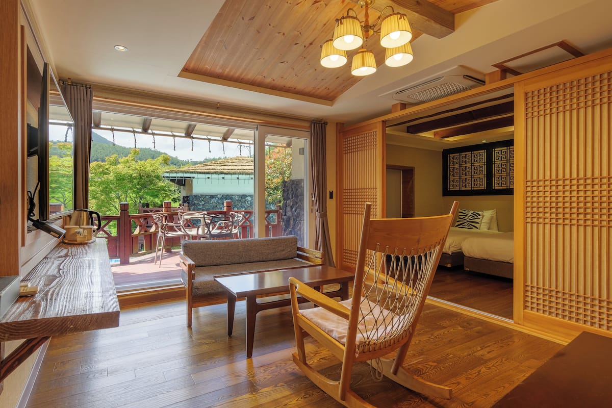 A spacious room with a wooden floor, a large window offering a view of the outdoors, a seating area with a sofa and chairs, and a traditional Japanese sliding door.