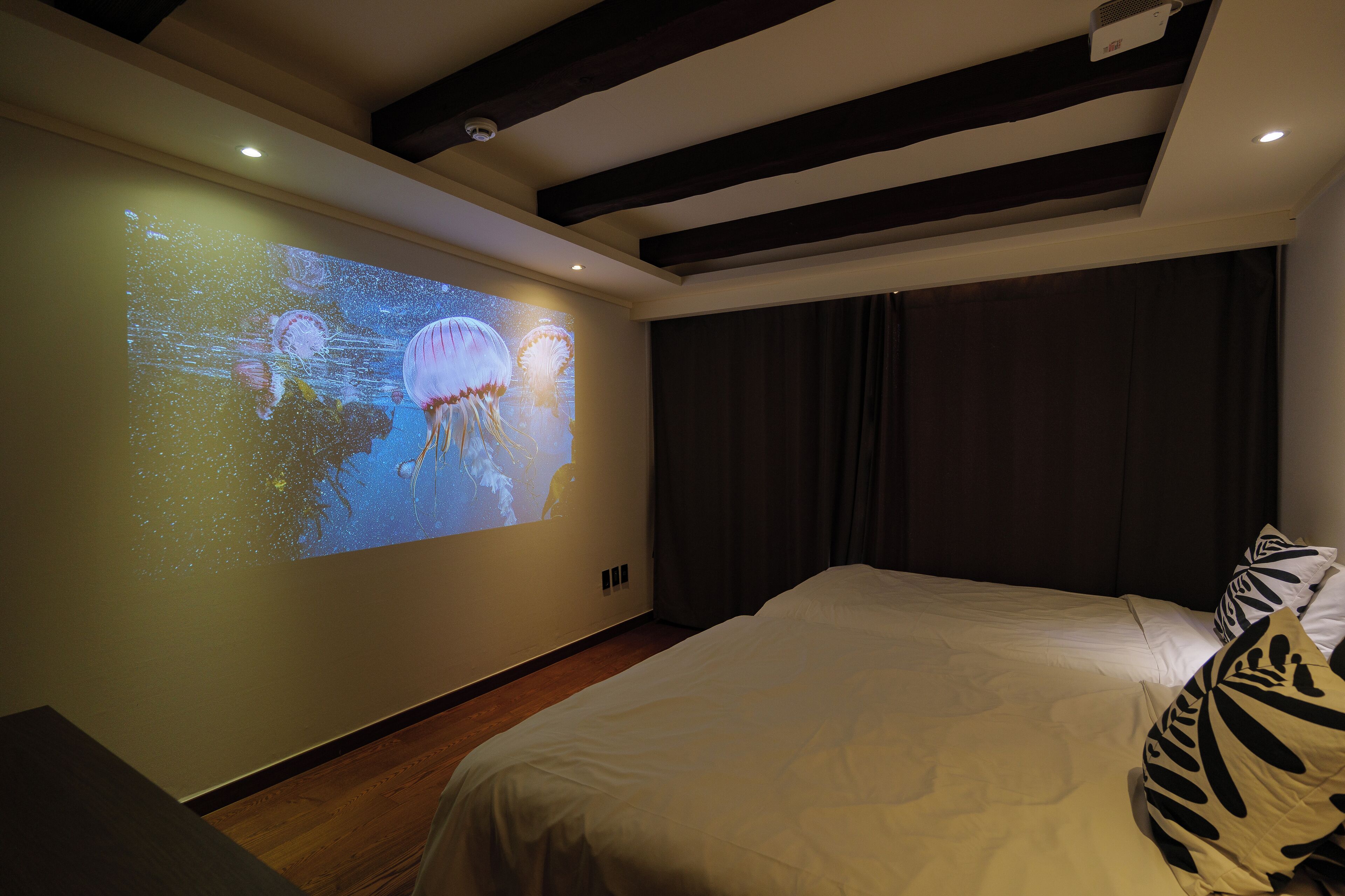 A bedroom with a bed, a large screen displaying an image, and a dark curtain.