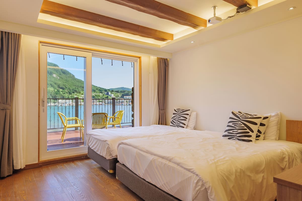 A hotel room with a large bed, a balcony with chairs, and a scenic view of hills and water.
