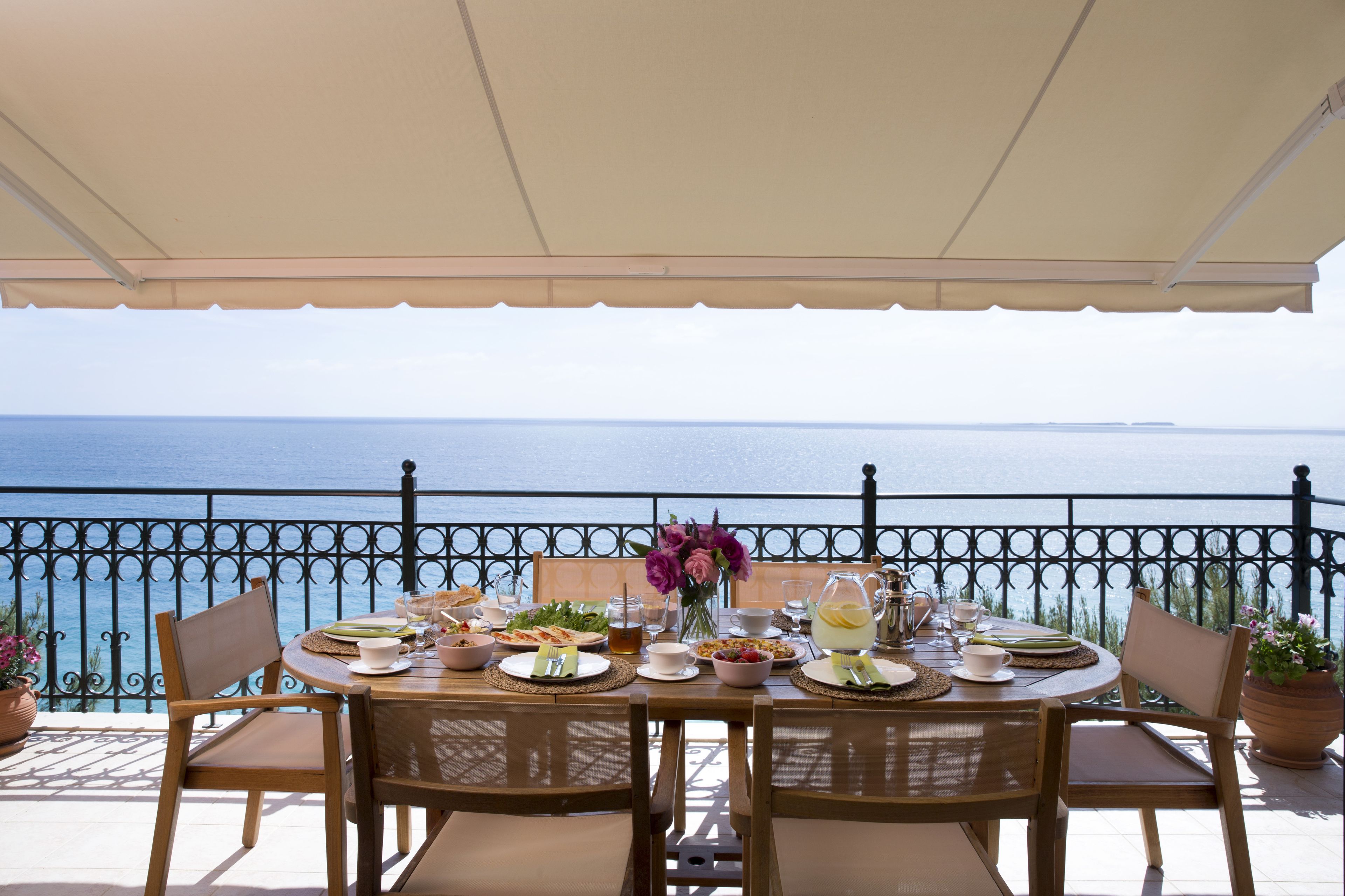 Ein Tisch, gedeckt für eine Mahlzeit, mit Blick auf das Meer, umgeben von Stühlen und einer Brüstung.