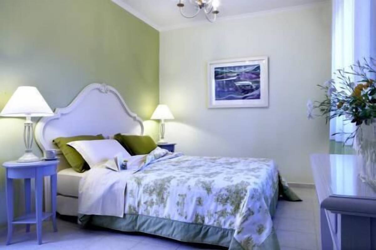 A bedroom with a bed, two bedside tables with lamps, a framed picture on the wall, and a window with a view.