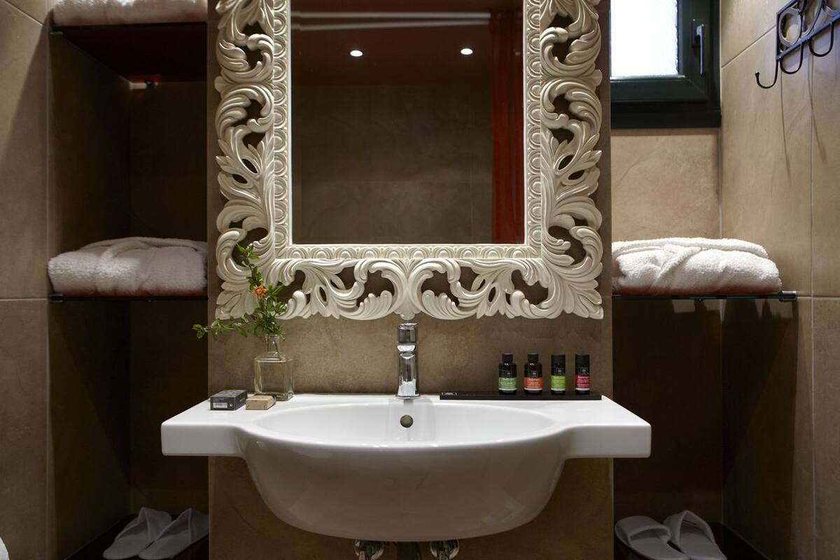 A bathroom with a large ornate mirror, a white sink, and a shelf with toiletries.