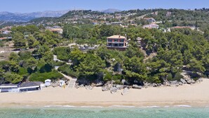 Una propiedad costera con playa, aguas cristalinas y montañas al fondo.